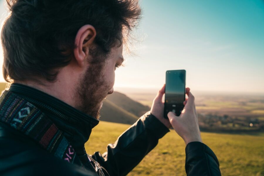Hiker holding smartphone under clear sky mountains